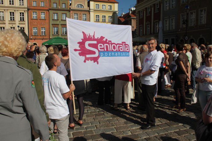 Na zdjęciu wolontariusze Centrum Inicjatyw Senioralnych podczas inauguracji „Senioraliów” na Starym Rynku. Trzymają duży baner z napisem” Senioralia poznańskie”. 