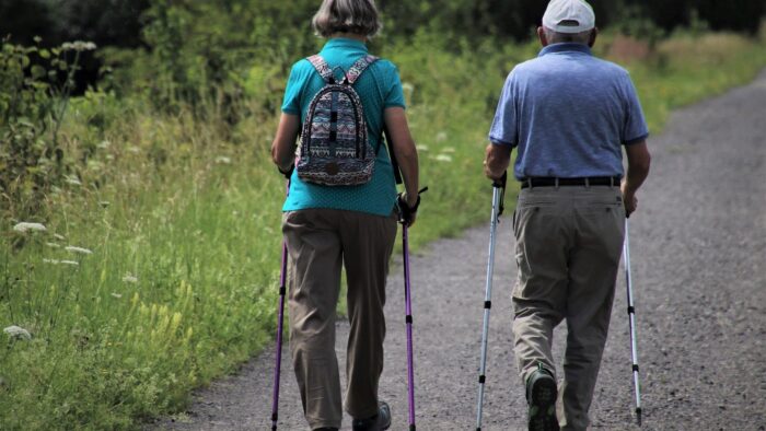 Grafika artykułu: Na zdjęciu dwoje seniorów z kijkami do nordic walkingu, tyłem do obiektywu.