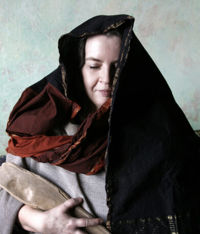 Grafika artykułu: na zdjęciu artystka w stroju bretońskim, trzyma w reku drewniany przedmiot, na głowie ma chustę, ma zamknięte oczy.