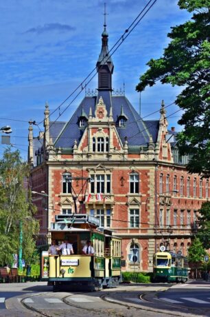 Grafika artykułu: zdjęcie zabytkowego tramwaju poznańskiego w kremowo-zielonym kolorze. W tle czerwony budynek na placu Cyryla.