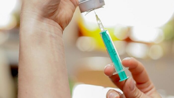 Grafika artykułu: Na zdjęciu widać dwie dłonie osoby, która przygotowuje szczepionkę, w centrum zdjęcia strzykawka.