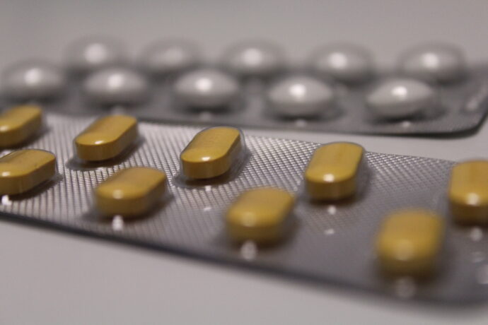 Grafika artykułu: Na biały stole leżą dwa listki tabletek - na pierwszym planie tabletki w kolorze żółtym, na drugim - w kolorze białym. 