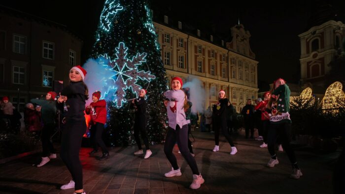 Grafika artykułu: Na zdjęciu grupa tancerzy w czapkach św. Mikołaja, w tle choinka.