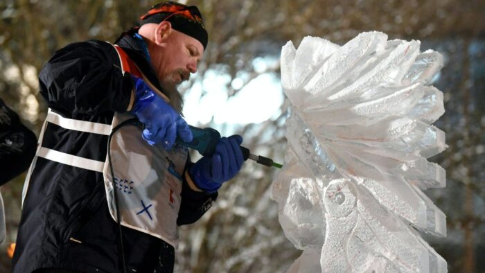 Grafika artykułu: Zdjęcie mężczyzny w zimowym ubraniu, stoi bokiem, w dłoniach trzyma narzędzie do rzeźbienia w lodzie. Po prawej stronie rzeźba lodowa.