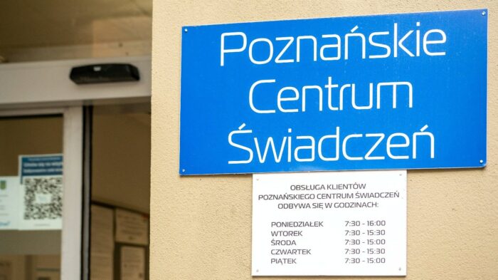 Grafika artykułu: w centrum na ścianie budynku niebieska tablica informacyjna z białym napisem: "Poznańskie Centrum Świadczeń", poniżej biała tablica z godzinami otwarcia.