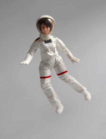 Grafika artykułu" Na szarym tle lalka Barbie w kombinezonie astronautki, unosi się w powietrzu. 