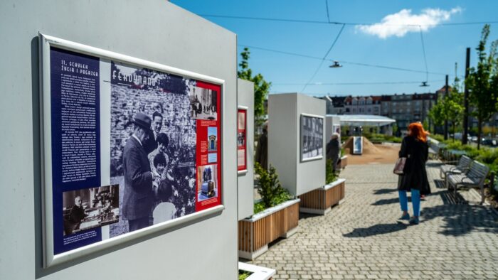 Grafika artykułu: na zdjęciu ekspozycja plenerowa o marszałku Fochu, na szarych filarach zawieszone są plansze wystawowe, w tle osoby oglądające wystawę.