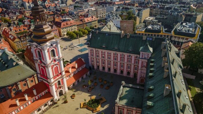 Zdjęcie przedstawia stary rynek i plac kolegiacki w Poznaniu. Fotografia robiona od góry ukazuje panoramę kolorowych budynków.