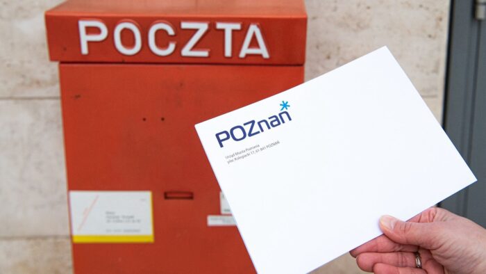 Zdjęcie koperty z logiem Poznania na tle czerwonej skrzynki na listy